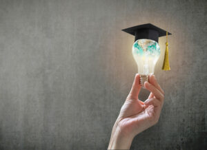 Hand holding a lit lightbulb with a graduation cap on it.