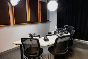 a podcast studio with sound panels on the walls, professional lighting, microphones, headsets, cameras, and four chairs